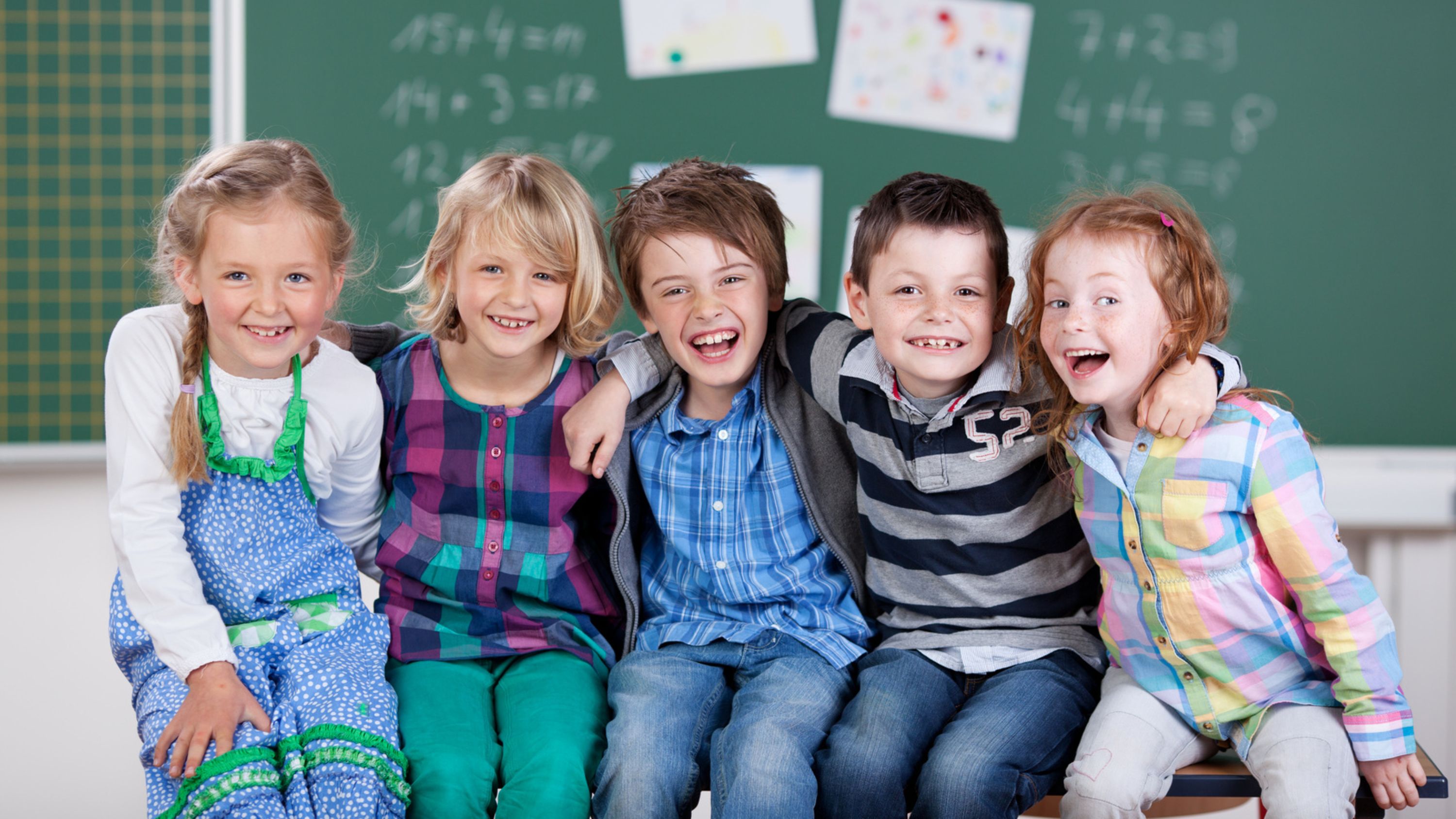 Schulkinder sitzen lachend vor einer Wandtafel