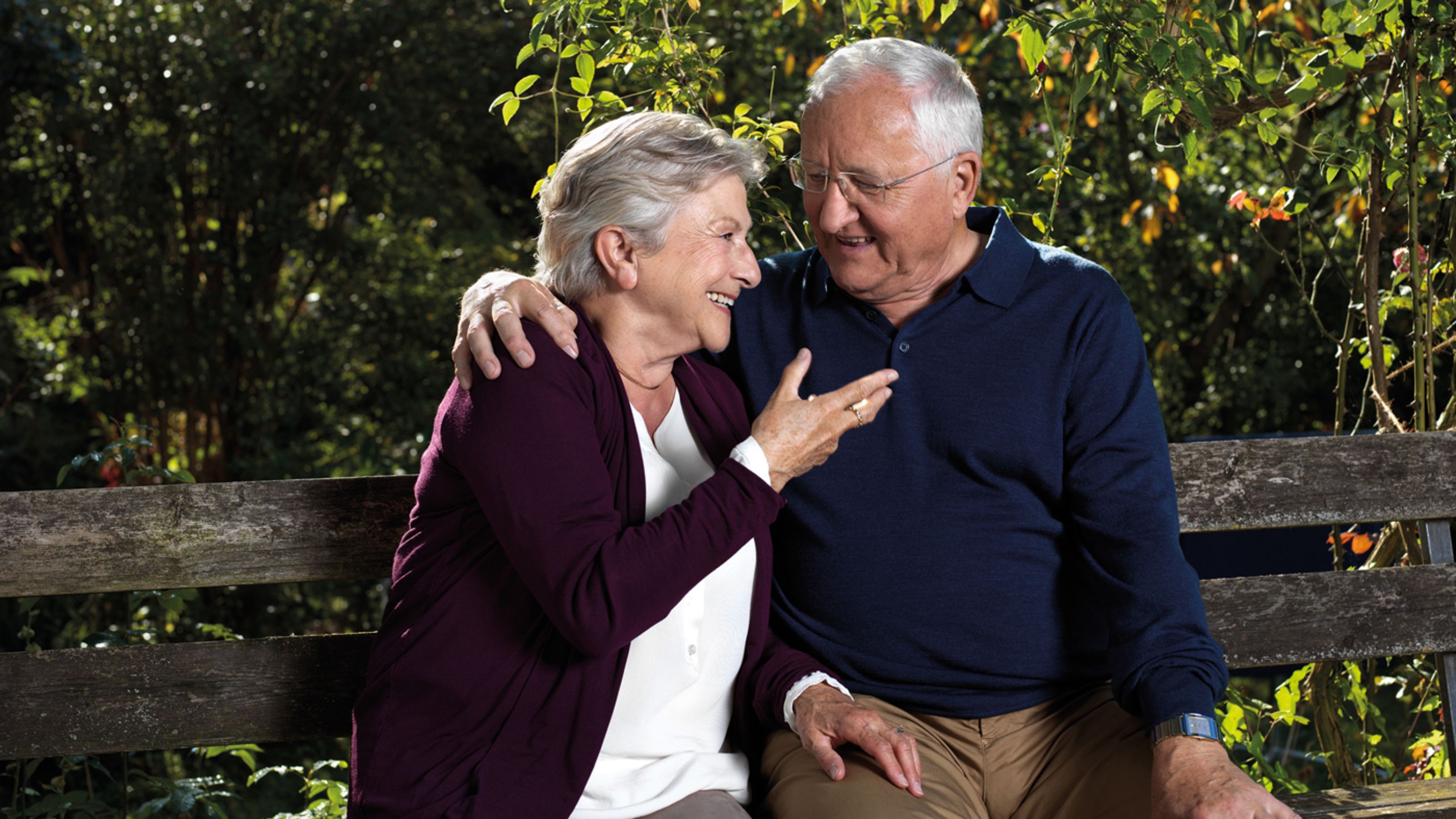 un couple de personnes âgées heureuses est assis sur un banc.