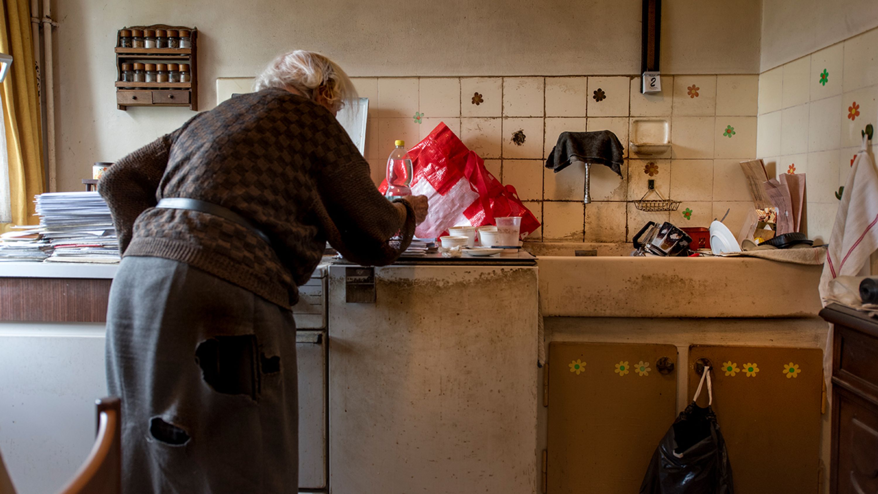 Una donna anziana che vive in povertà si china su un mobile della cucina.