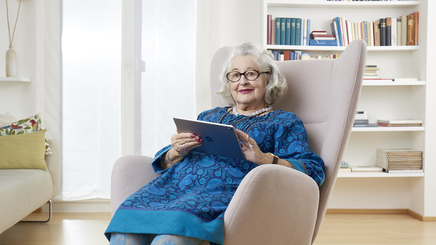 Une femme âgée regarde l'offre de Pro Senectute chez elle sur sa tablette.