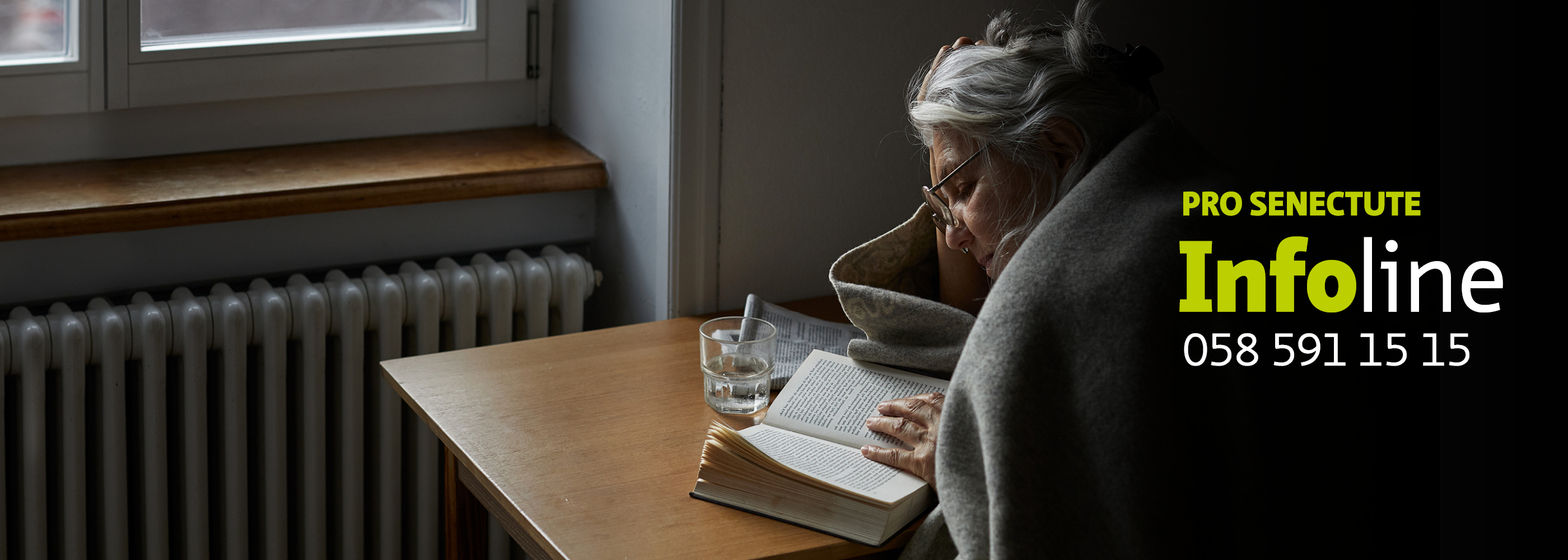Une dame âgée lit un livre, assise à son bureau avec une couverture et une tasse de thé.