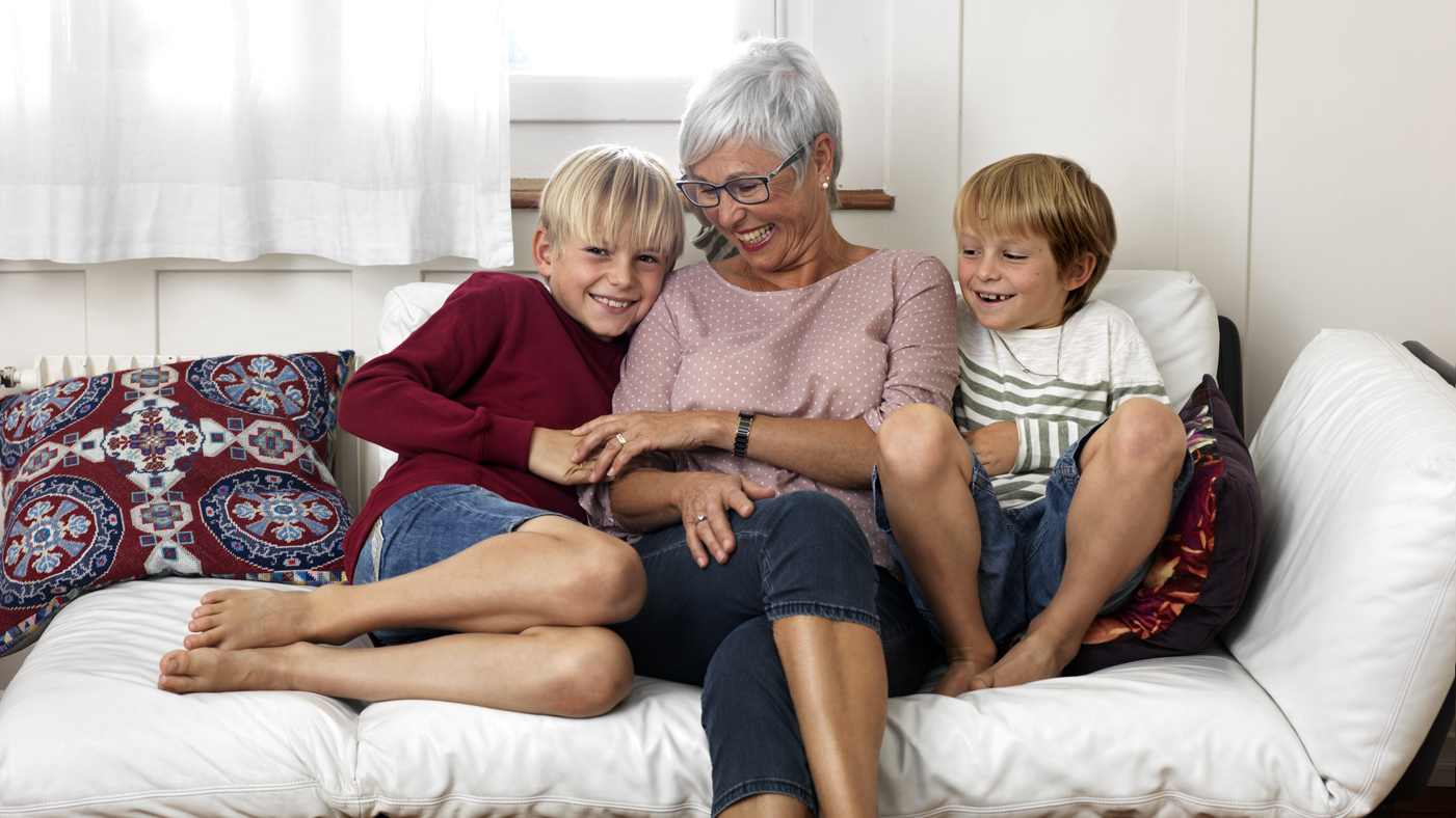 Eine ältere Frau sitzt fröhlich mit zwei Kindern auf einem Sofa