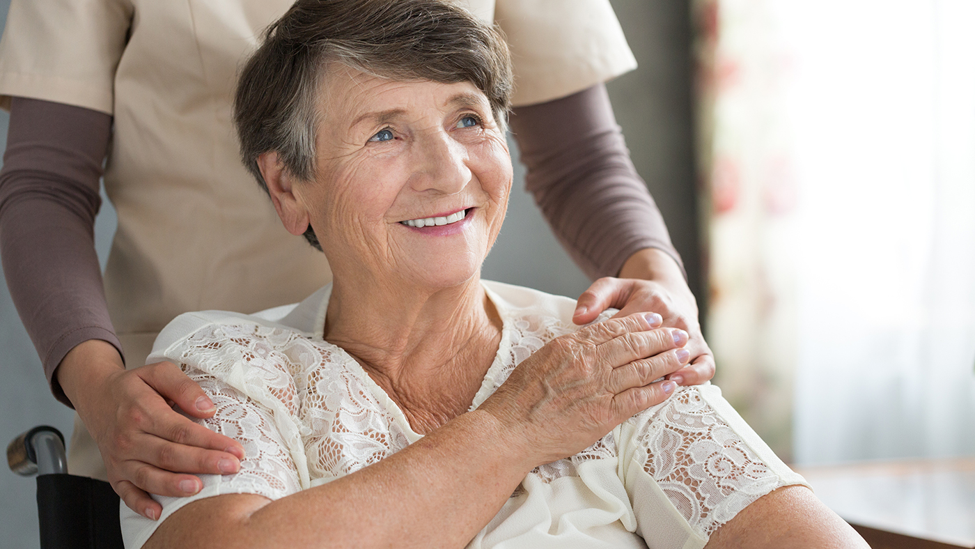 Une patiente âgée sourit et tient la main d'une aide-soignante.