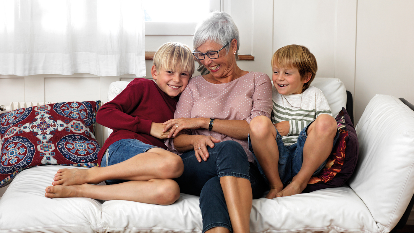 Eine ältere Frau sitzt mit zwei Kindern fröhlich auf einem Sofa