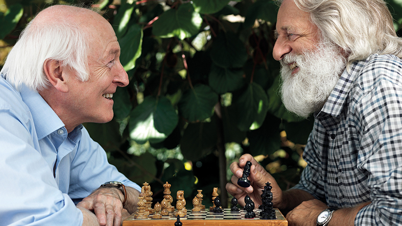 Zwei lachende Senioren beim Schachspiel.