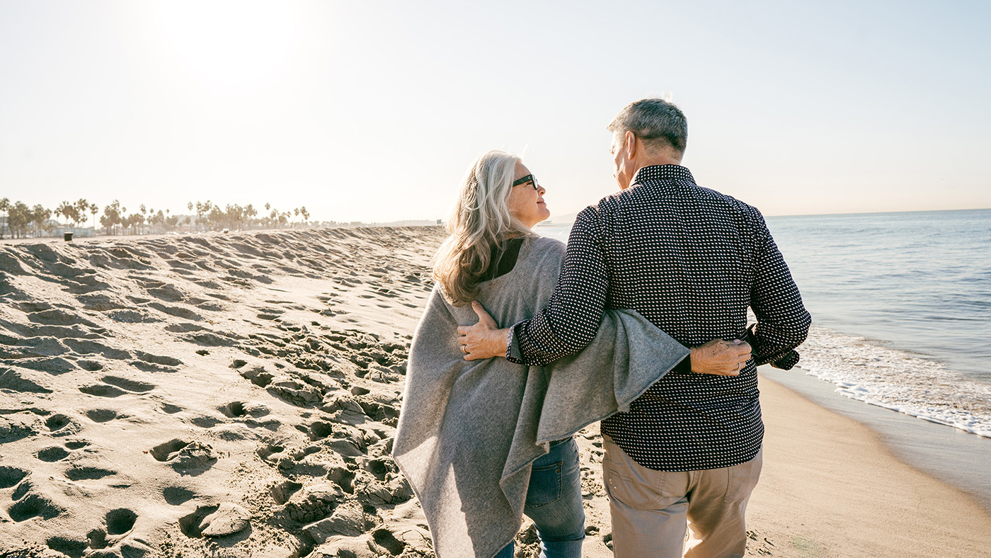 Couple âgé bras dessus bras dessous sur la plage.