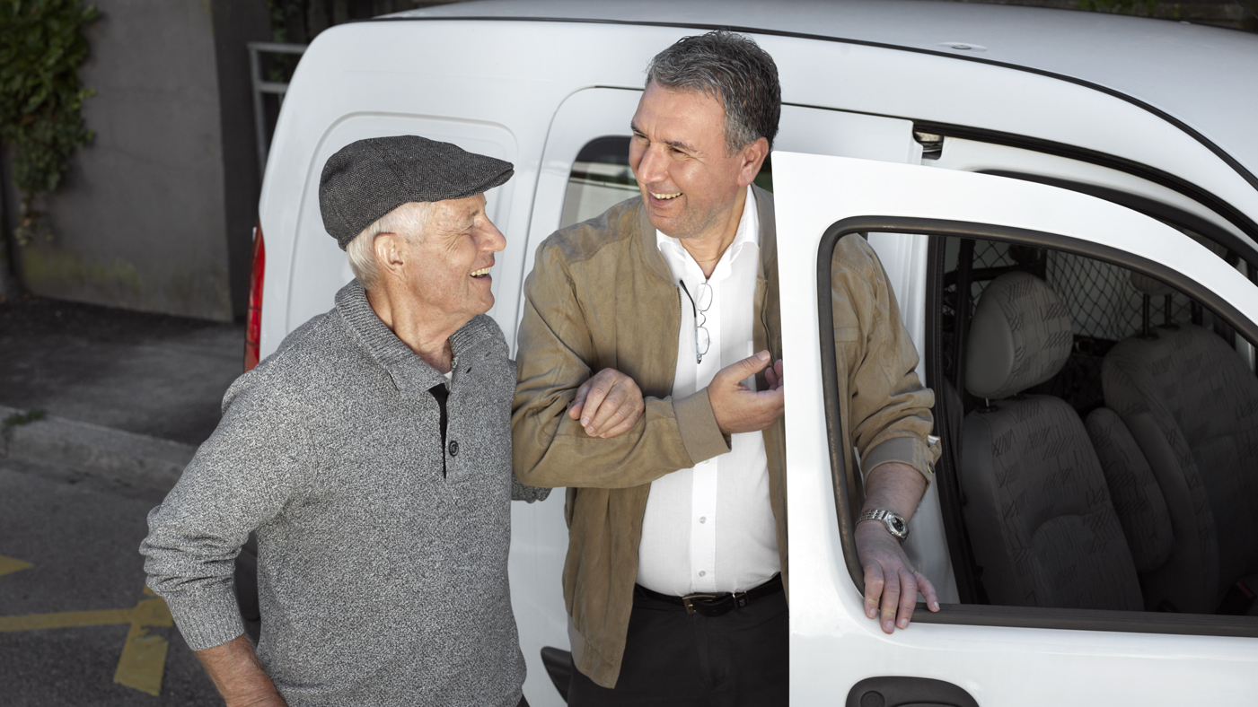 Ein Mann hilft einem Senior in ein Auto