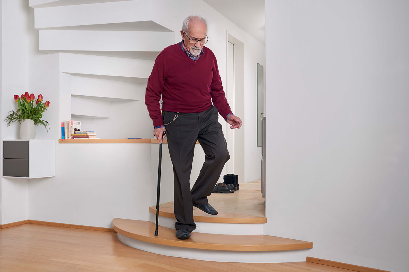 Un uomo anziano cammina con cautela giù per le scale con un bastone.