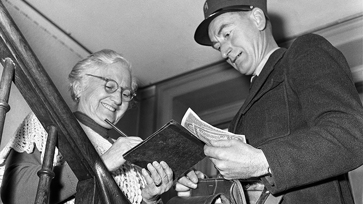 Ein Briefträger zahlt einer Rentnerin die AHV-Prämie aus, aufgenommen im Oktober 1955 (Bild: Keystone-SDA/Jules Vogt). 