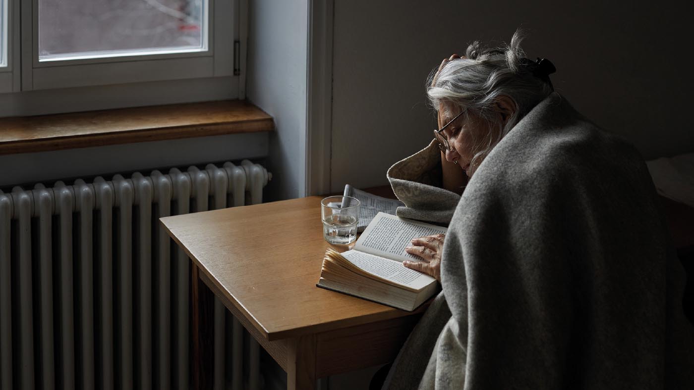 Un’anziana con una coperta e un tè legge un libro.