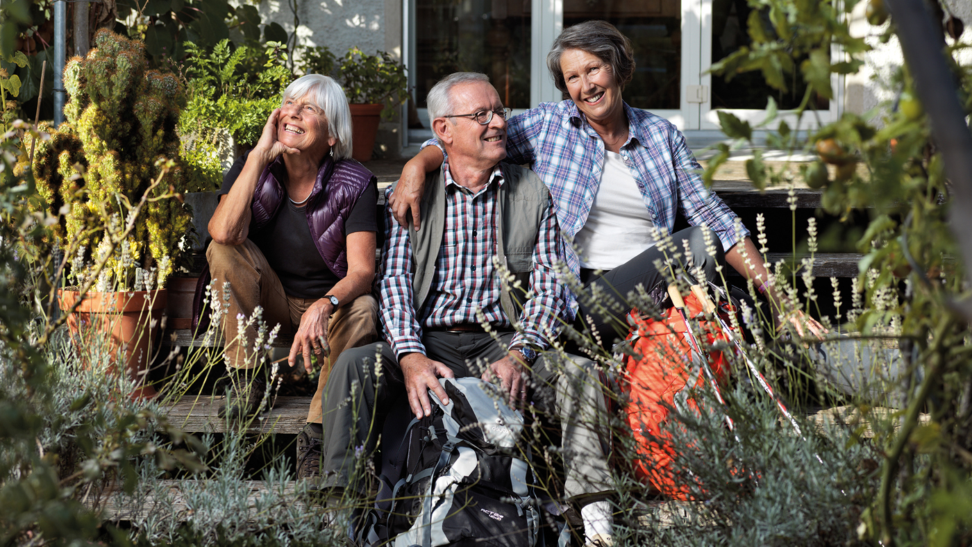 Zwei Seniorinnen und ein Senior sitzen lachend im Garten.