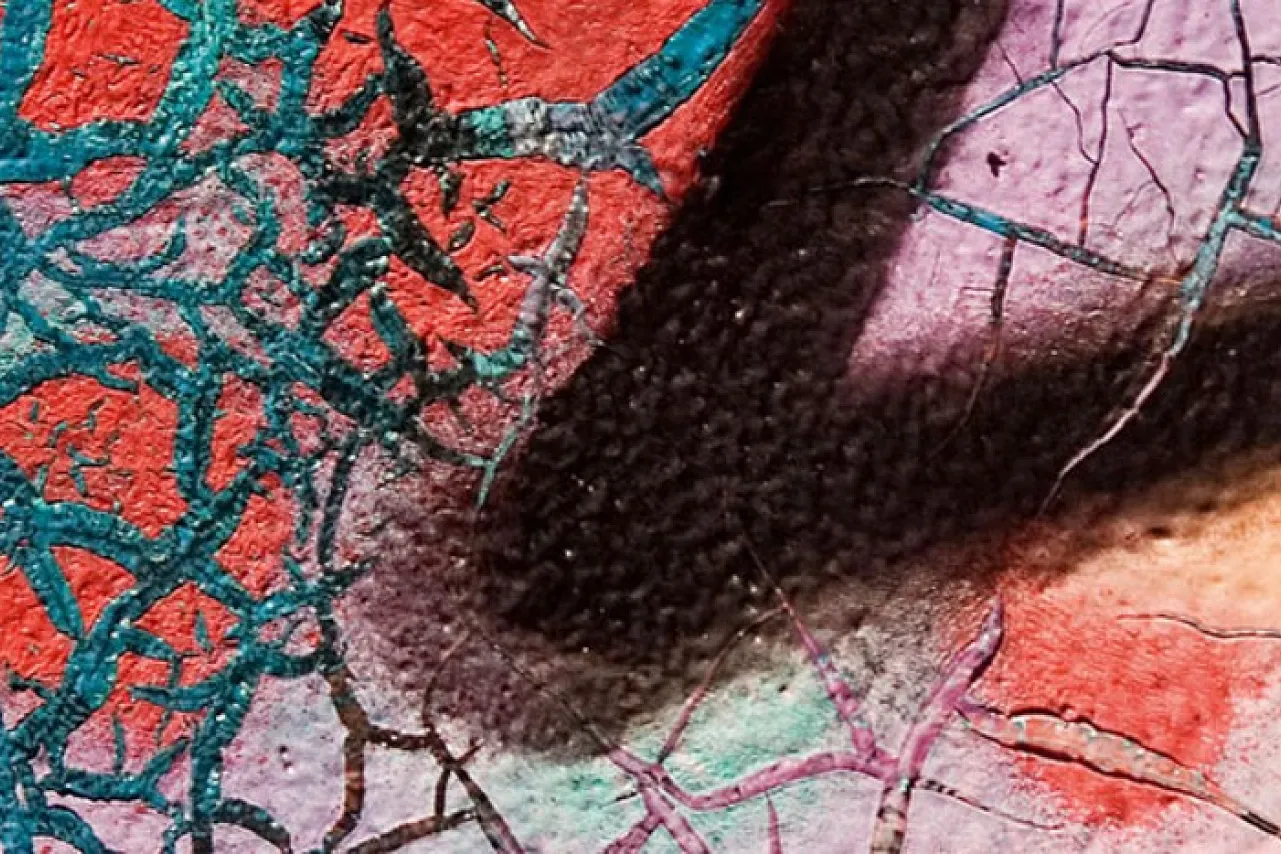 Das Bild zeigt einen Ausschnitt von bunter, stark verwitterter Wandkunst. Die rissige Oberfläche und die kräftigen Farben – Türkis, Rot, Violett und Schwarz – erzeugen eine spannende, fast abstrakte Textur.