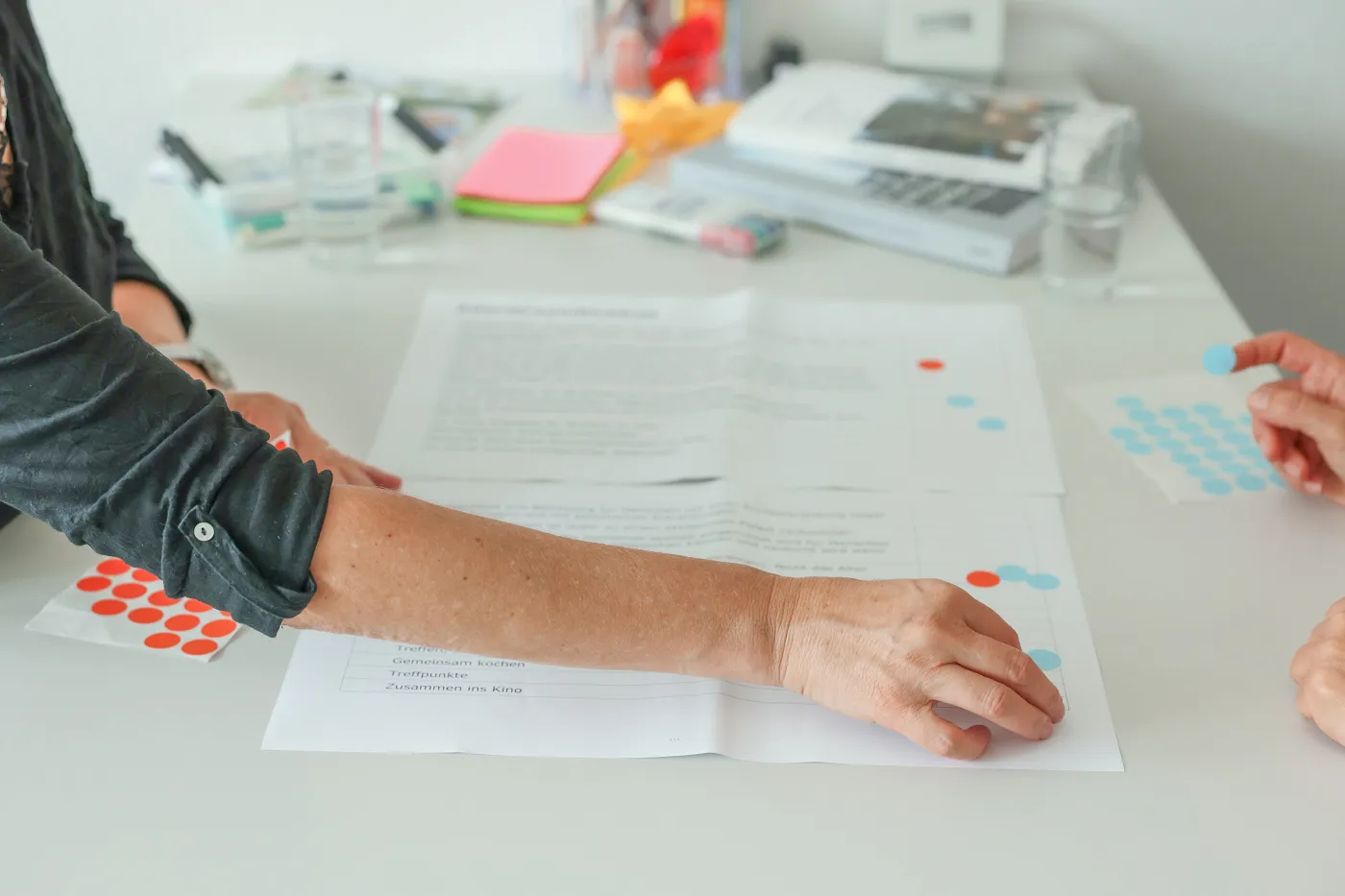 Personen ordnen ihre Ideen auf einem Blatt Papier nach Priorität, indem sie farbige Klebepunkte darauf kleben.