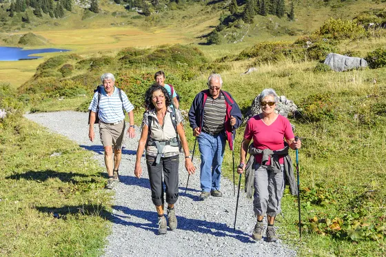 Bild fünf Personen wandern auf einem Bergwanderweg aufwärts. Im Hintergrund ist ein tief blauer Bergsee.