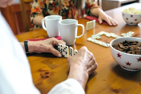 Bild an einem Holztisch spielen Hände Domino zwischen Kaffeetassen und Schalen mit Keksen.