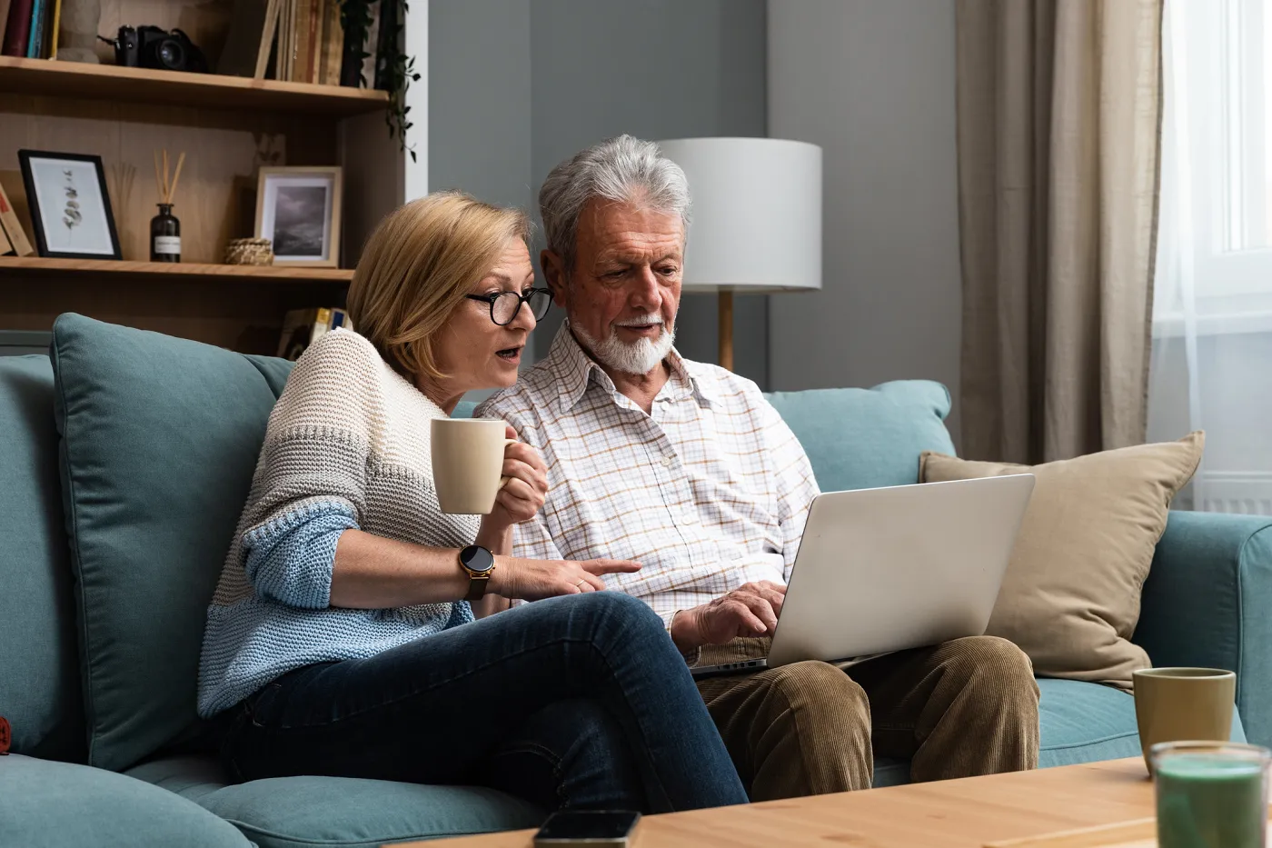 Bild ein Mann und eine Frau sitzen auf einem blauen Sofa. Die Frau hält eine Tasse in der Hand und der Mann hat einen Laptop auf den Knien. Gemeinsam schauen sie sich im Laptop etwas an.
