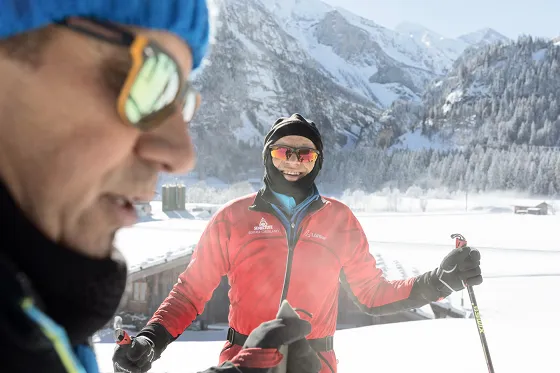 Bild verschneite Winterlandschaft in den Bergen. Ein Skilehrer in rotem Overall gibt Anweisungen.