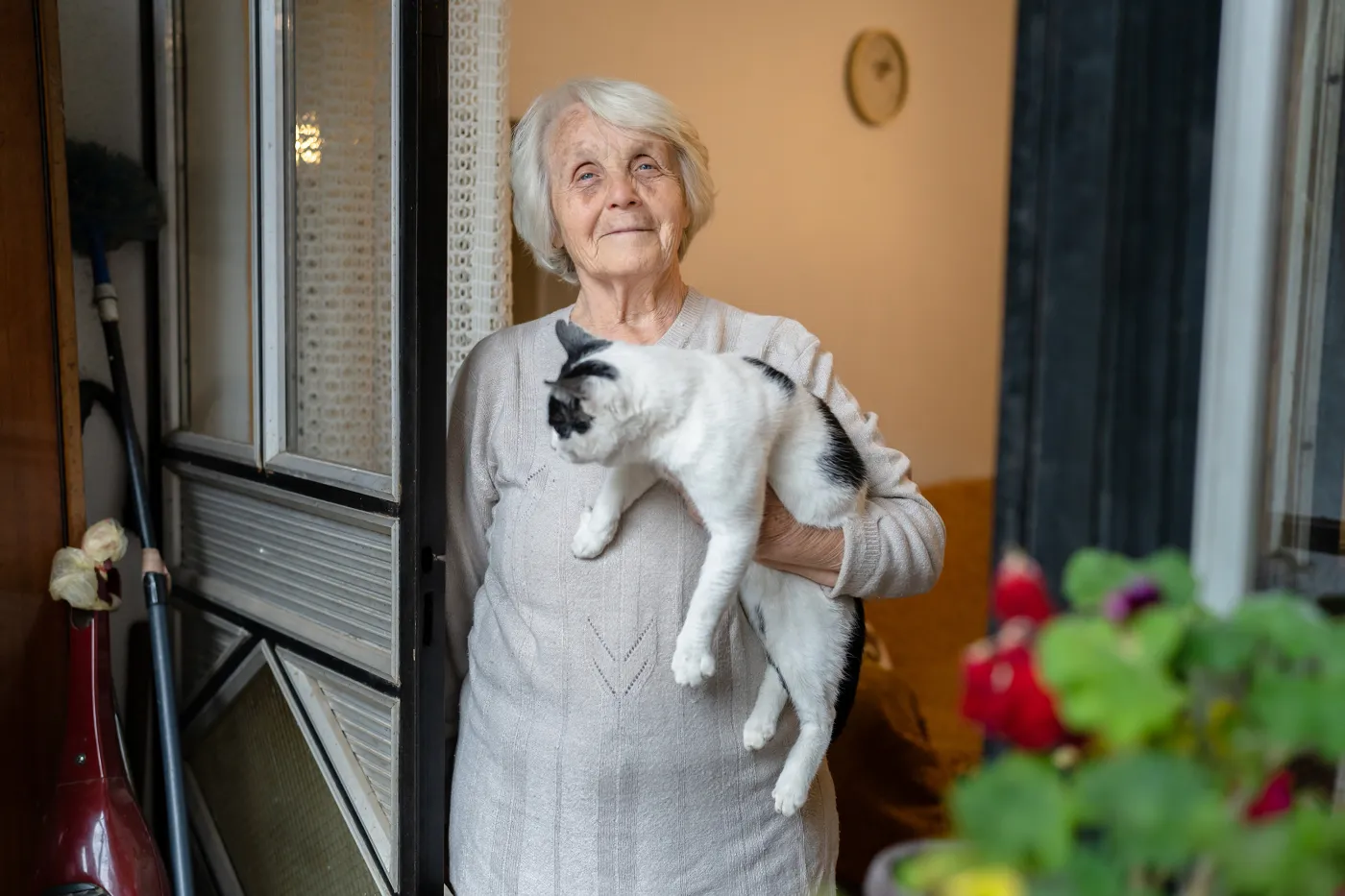 Das Foto zeigt eine ältere Frau, die eine Katze mit einer Hand an ihre Brust drückt und nachdenklich wirkt.