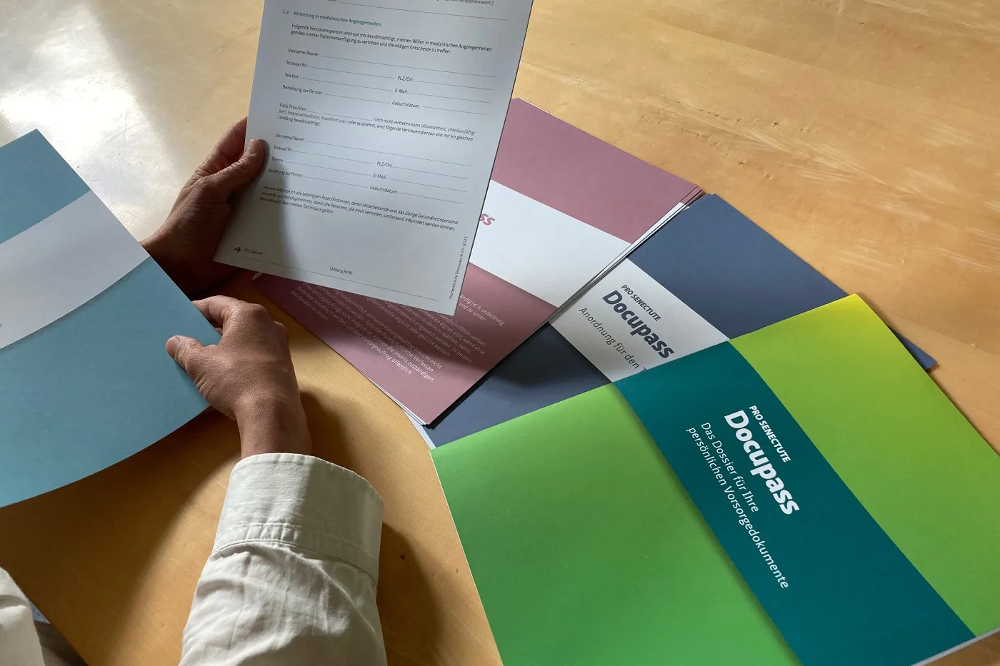 Bild eine Hand hält einen Formular aus dem Docupass in der Hand. Die übrigen Docupass-Unterlagen liegen auf dem Tisch.