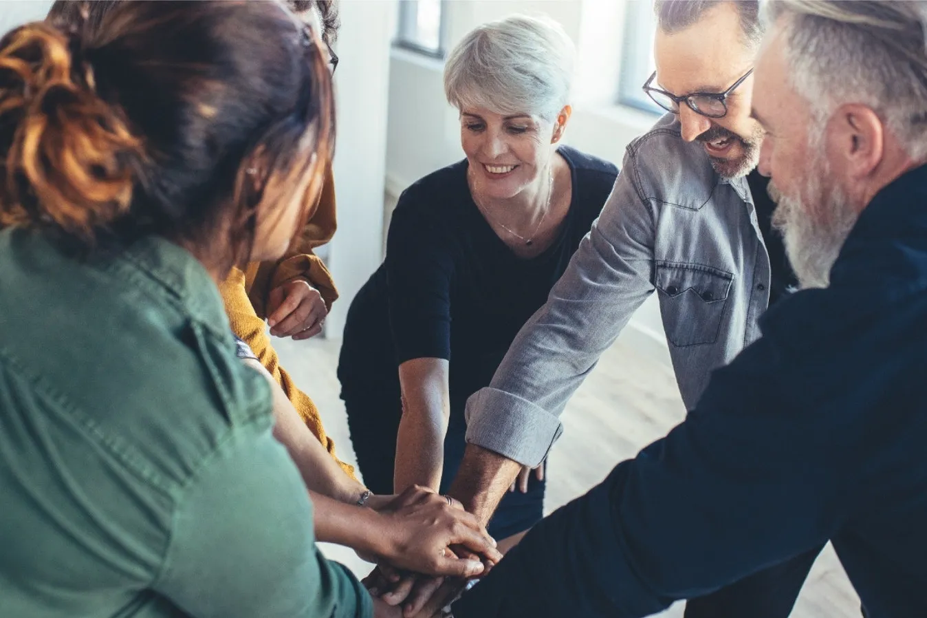 Bild fünf Personen stehen leicht nach vorne gebeugt im Kreis und legen in der Mitte des Kreises die Hände aufeinander