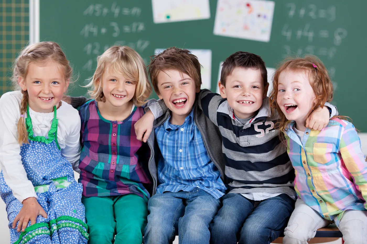 Photo trois filles et deux garçons assis sur un banc devant le tableau noir de la salle de classe