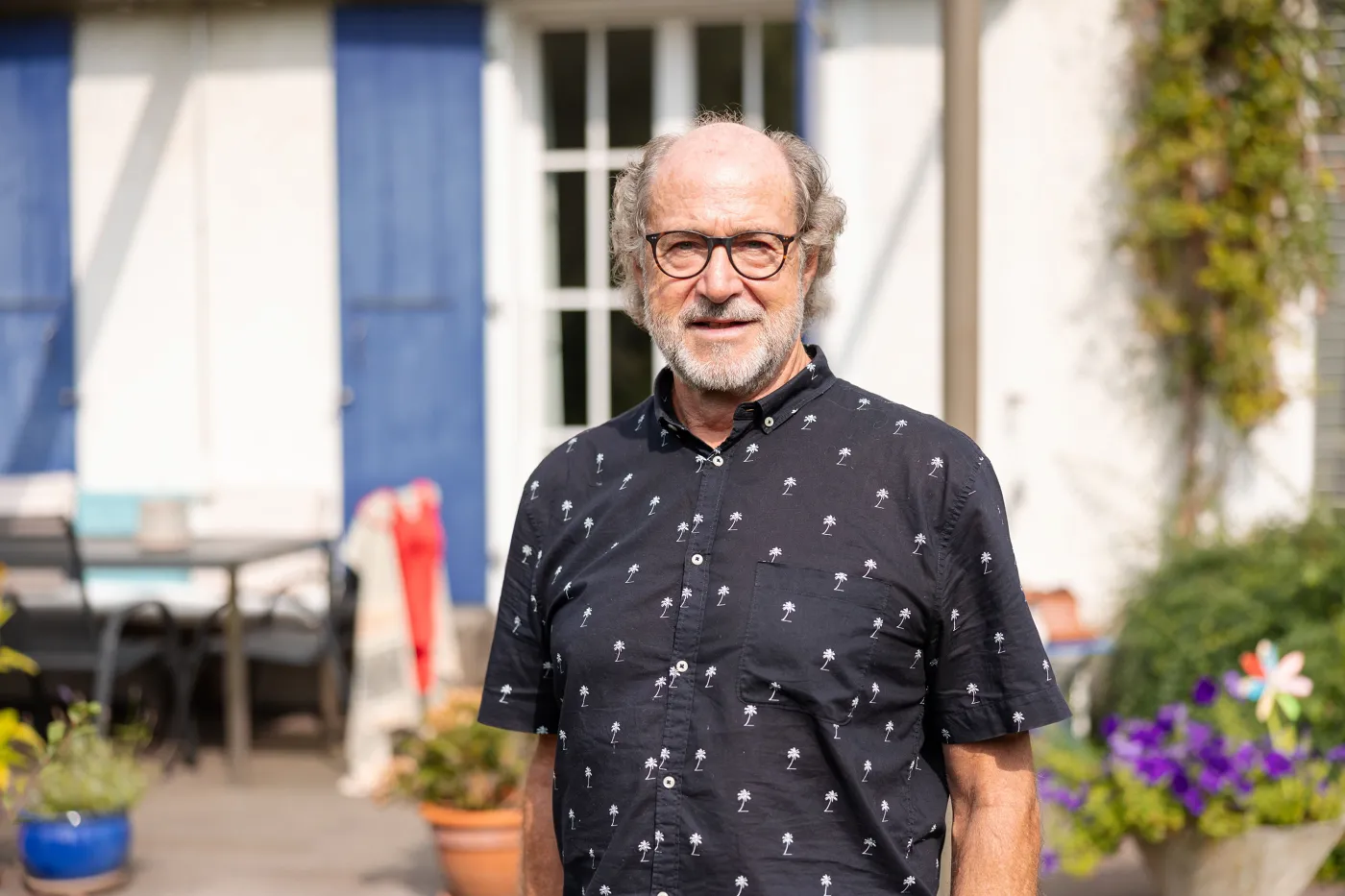 Il s'agit d'un portrait d'Alib Saner, vêtu d'une chemise estivale, debout devant une maison.
