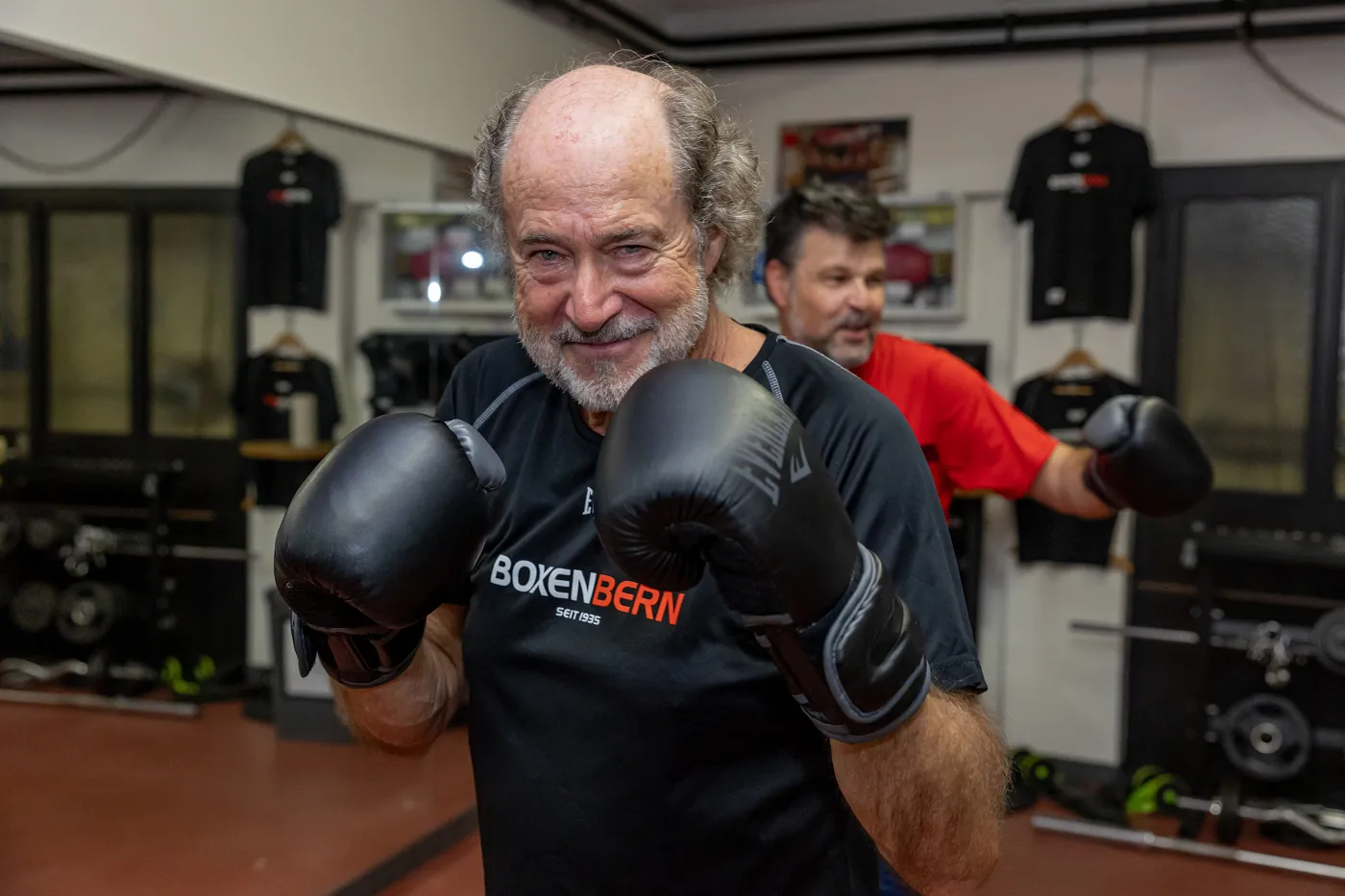 Image: Albi Saner se trouve dans la salle de boxe et porte des gants de boxe tout en souriant à la caméra.