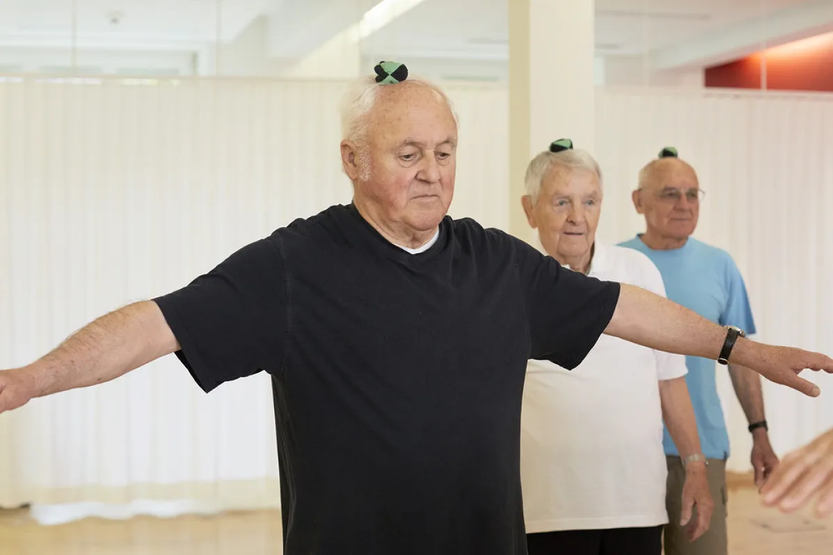 Image trois hommes debout avec une petite balle sur la tête. Ils essaient de garder l'équilibre, en partie avec les bras tendus sur le côté.