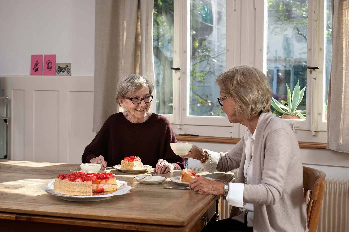 Image Deux femmes sont assises à une table en bois. Elles boivent du café et mangent une tarte aux fraises. Elles discutent.